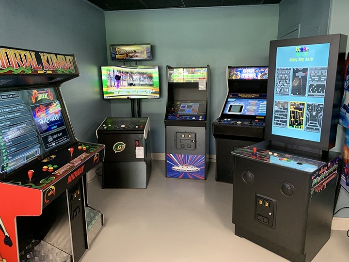 Photo of multiple game machines inlcuding Mortal Kombat, Golden Tee and Arcade Legends inside a man cave.