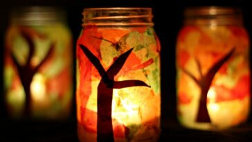 Mason jars decorated with tree branches, colorful tissue paper, and lit candles.