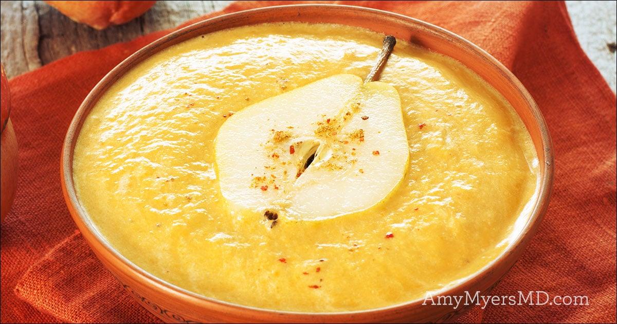 Yellow soup in an orange dish with a pear in the middle.