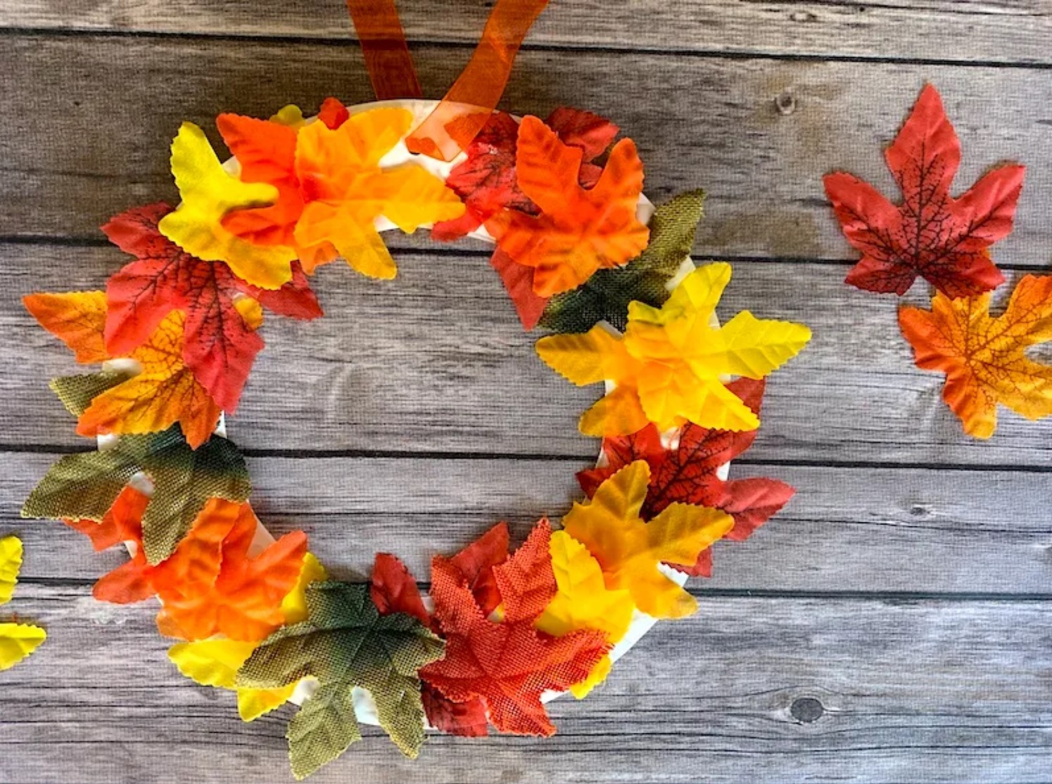 Wreath of yellow, green, red, and orange leaves on a wood background in honor of Fall.