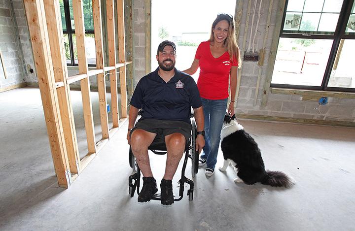 Photo of one of our veteran heroes smiling with woman and dog standing in a house being built, courtesy of Building Homes for Heroes.